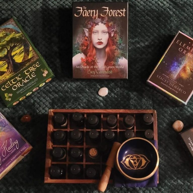 Oracle cards in a semi circle surrounding a box of essential oils and a crown chakra singing bowl.